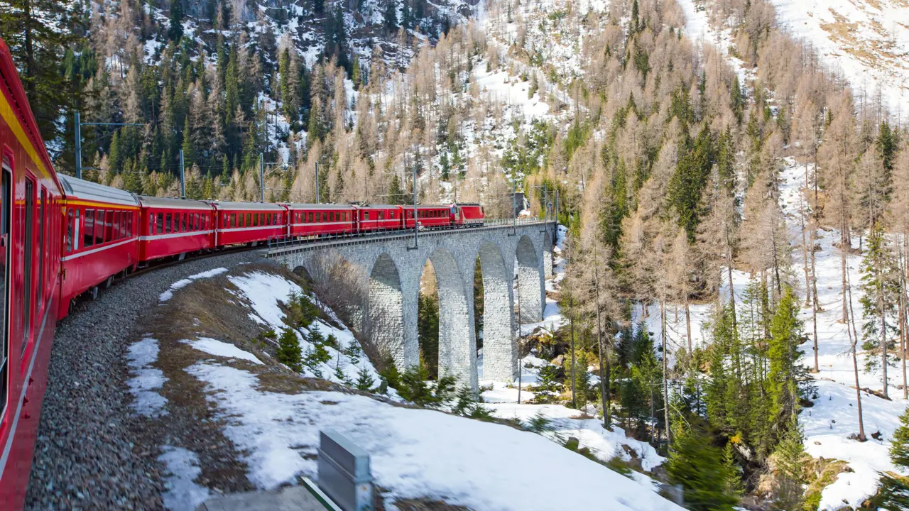 The Bernina Express going along the railway in the mountains, in the snow