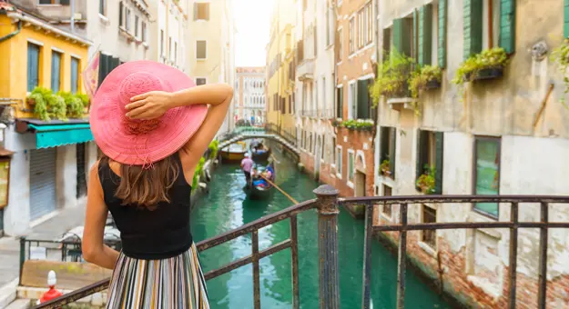 Back of a lady looking over a canal in Venice, with a gondola travelling down it and buildings either side